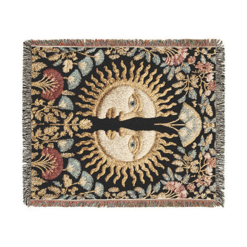 Jacquard-woven cotton blanket featuring twin celestial suns—two serene faces meeting at center—with radiant golden rays on a charcoal ground, bordered by folkloric botanicals and fan blossoms in sage, sky, and garnet. Crafted from 100% soft cotton yarn; the artwork is woven, not printed. Reversible with a color-negative back and finished with a protective 2-inch multicolor fringe. Sizes: 52×37, 50×60, 60×80 for wall, sofa, or queen-bed layering.